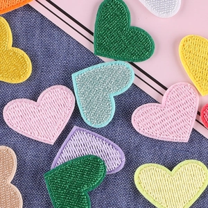 Colorful embroidered heart patches in various pastel tones on denim and pink background