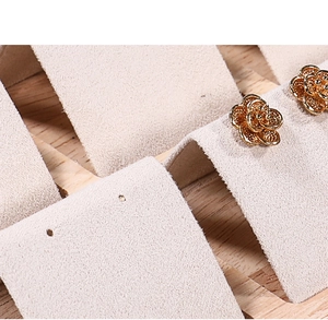 Detailed close-up of golden rose flower stud earrings on a beige velvet display stand