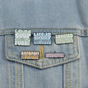 Close-up of five colorful enamel letter pins with funny quotes on denim jacket