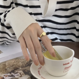Close-up of a minimalist gold signet ring worn by a model holding a white coffee cup