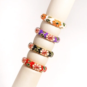Detail of four colorful enamel flower rings in white, purple, black and red on a jewelry stand
