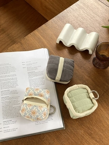 Three fabric zipper earphone pouches in grey green and floral patterns on a wooden desk