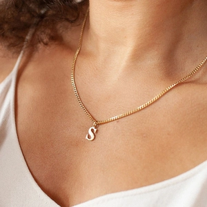 Golden necklace featuring a stylish letter S pendant worn by a model in a natural setting