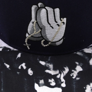 Detail of navy baseball cap featuring 3D praying hands embroidery and printed brim
