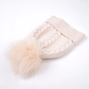 Gros plan du bonnet en tricot crème avec motif torsadé et pompon en fausse fourrure