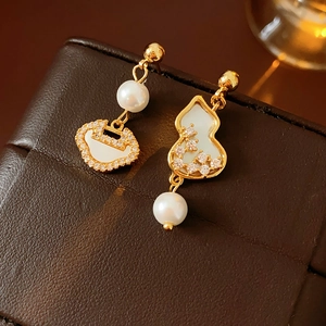 Detailed view of asymmetric gold earrings with zircon, gourd, and pearl elements