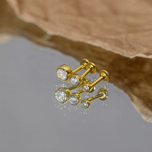 Macro detail of three gold stud earrings with round cubic zirconia on reflective surface