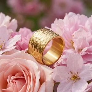 Close-up of golden wide band ring with hammered texture among pink roses and cherry blossoms