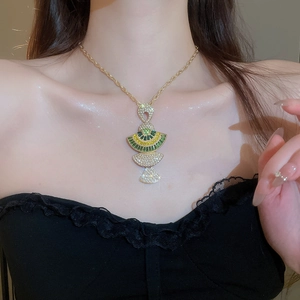 Detail of luxury gold fan necklace with green and yellow gems on model neck