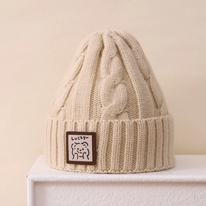 Detail of cable knit pattern and brown patch with cute bear on a beige winter hat