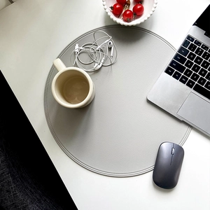 Gray round faux leather placemat with stitched edges on a minimalist office desk