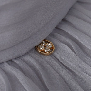Macro detail of sun hat showing a gold clover buckle with rhinestones on grey fabric