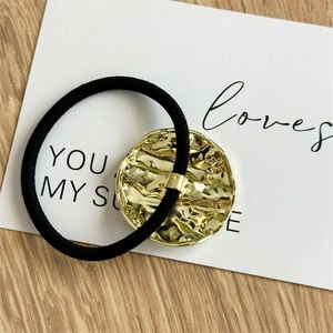 Detail of irregular textured golden metal charm on minimalist black elastic hair tie