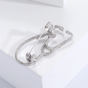 Macro shot of a creative silver stethoscope brooch displayed on a white studio pedestal