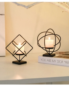 Close-up of geometric black iron candle holders with warm pillar candles on a dining table