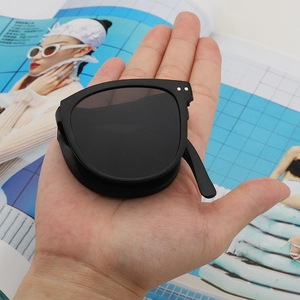 Foldable black sunglasses being held in a palm to show compact size and portability