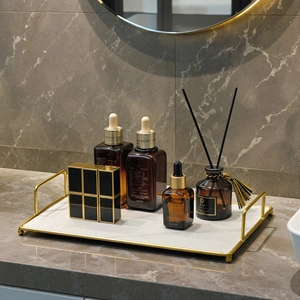 Golden metal frame bathroom tray with marble base holding luxury skincare serum bottles