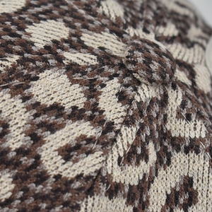 Close-up of thick knitted winter hat with vintage brown leopard jacquard pattern and top button