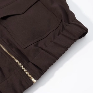 Detailed macro view of dark brown fabric with a gold metal zipper and elastic cuff