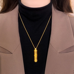 Dettaglio di una collana con pendente a cilindro dorato traforato indossata su un blazer