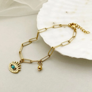 Macro detail of gold paperclip chain bracelet with evil eye and turquoise bead charms