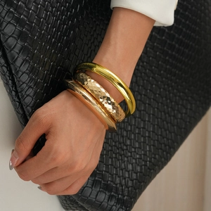 Close-up of stacked gold bangles with smooth and embossed textures on a model wrist