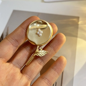 Détail d'une broche fleur en or mat vintage avec perles tenue à la main sur un livre