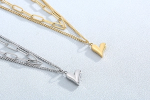Détails des colliers superposés en or et argent avec pendentifs cœur sur fond bleu