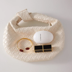 Detail of a gold stainless steel bangle with red agate inlay paired with a cream woven bag