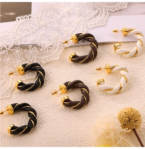 Detail of twisted C-shaped earrings with woven leather texture in gold and brown tones
