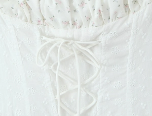 Détail d'une robe en broderie anglaise blanche avec bordure fleurie rose et laçage avant