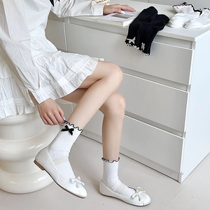 Detailed view of white Lolita style socks with black bows and frilled cuffs worn by model