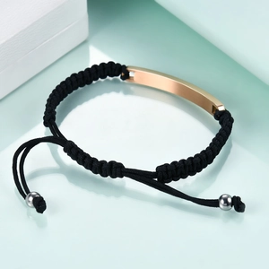 Macro shot of a black braided rope bracelet featuring a polished rose gold metal bar