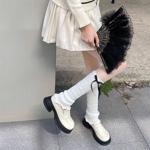 Detailed knit texture of cream leg warmers with black ribbon bows in balletcore style