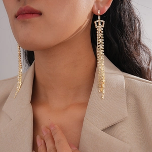 Close-up of golden tassel earrings with sparkling crystals and crown detail on model