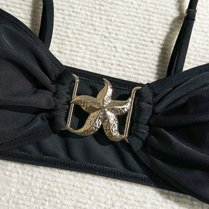 Dettaglio del top bikini nero con fibbia in metallo dorato a forma di stella marina