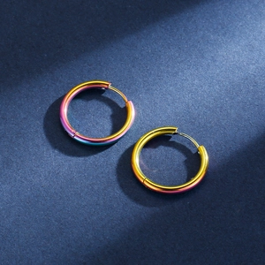 Close-up of rainbow gradient stainless steel hoop earrings on textured blue surface
