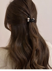 Détail d'une petite pince à cheveux noire avec perles sur cheveux bruns bouclés style élégant