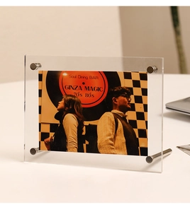 Detailed side view of clear acrylic photo frame with silver metal support screws on a desk