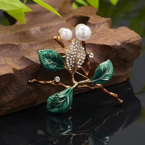 Detail of enamel branch brooch with green leaves and white pearls on wooden base