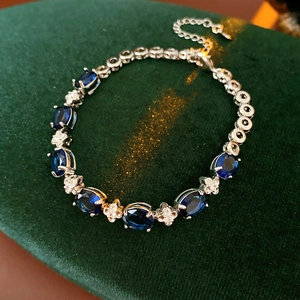 Macro detail of dark blue oval gemstone bracelet with cross diamond accents on green velvet