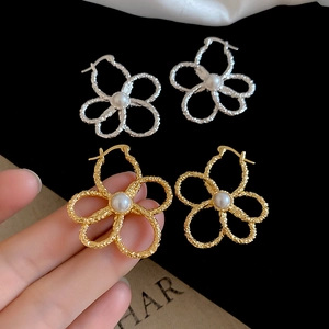 Detailed view of metal flower earrings with pearl centers in gold and silver finish