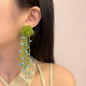 Handmade beaded flower tassel earrings with green and light blue crystals on a model
