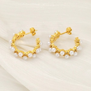 Detail of C-shaped gold-plated earrings with white pearls on a silk fabric background