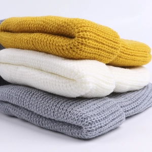 Stack of knit beanies in yellow white and grey colors for autumn and winter warmth