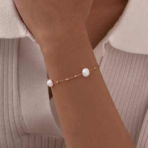 Detailed view of elegant gold-plated bracelet with white pearls worn on a woman's wrist