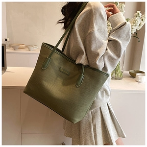 Detail of dark green woven tote bag with metallic logo tag and dual shoulder straps
