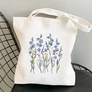 Weiße Canvas-Einkaufstasche mit blauen Blumen-Aquarellen auf einem modernen Metallstuhl