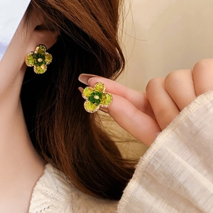Détail des boucles d'oreilles fleur à quatre pétales avec cristaux verts et dorés