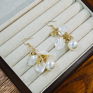 Detail of elegant gold earrings with white acrylic petals and large artificial pearls